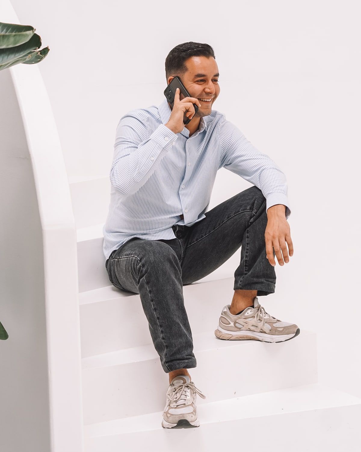 Mo zit lachend op een witte trap en belt met zijn telefoon