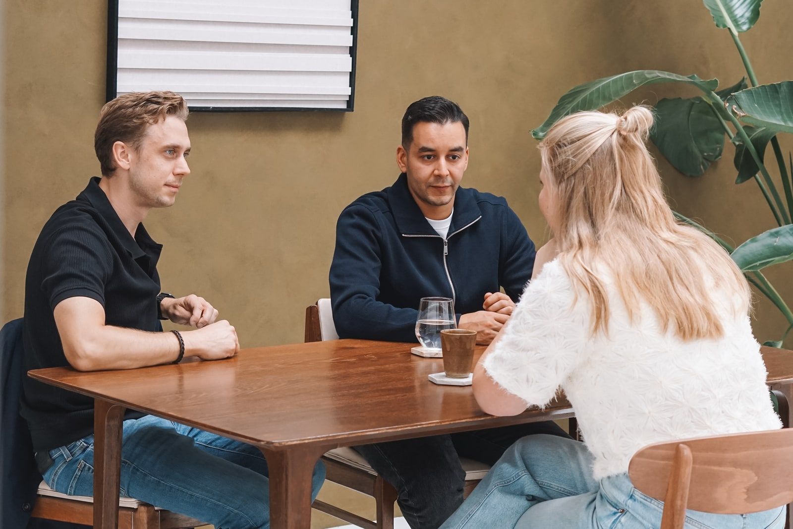 Paul en Mo in gesprek aan een houten tafel, met tegenover hen een gesprekspartner