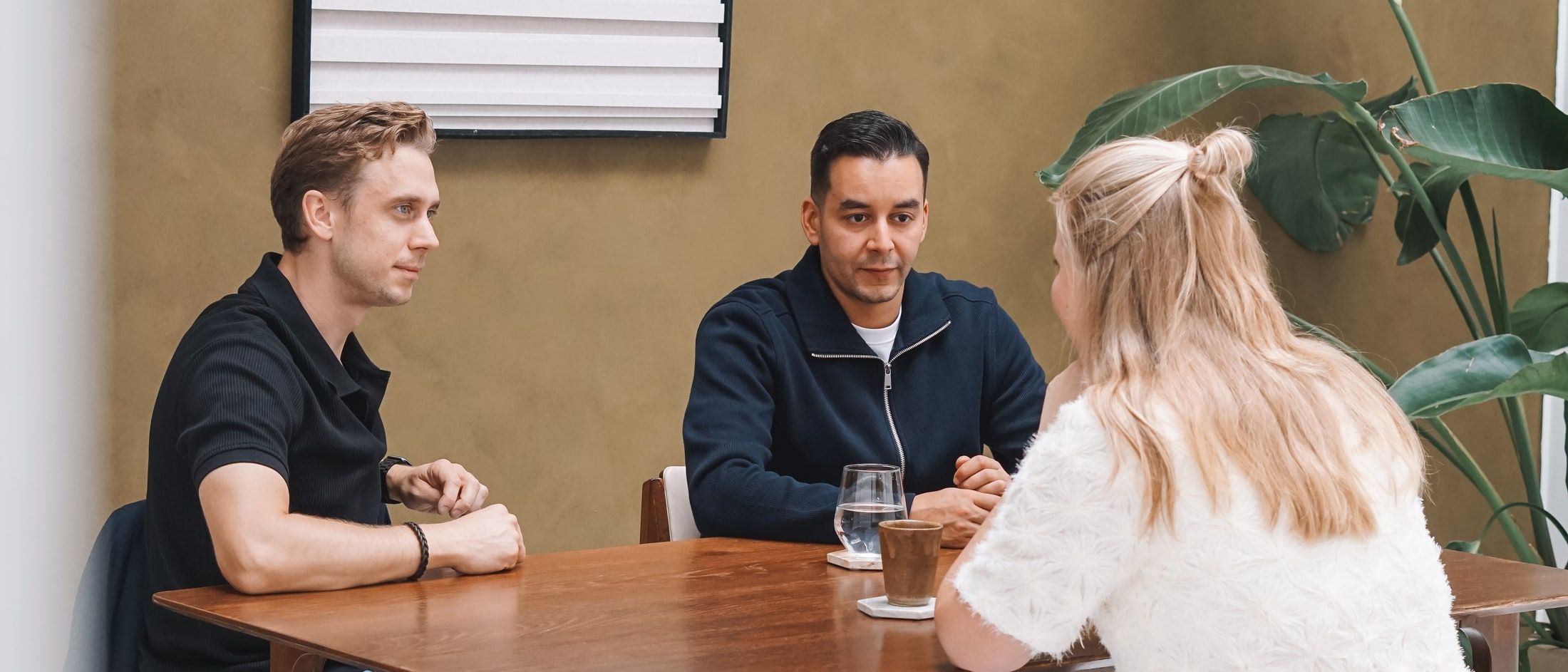 Paul en Mo in gesprek aan een houten tafel, met tegenover hen een gesprekspartner